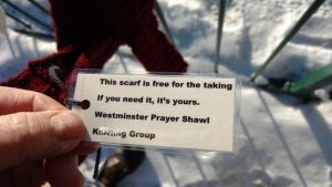 Picture of prayer shawl tied to fence with tag saying it's free to take if you need one